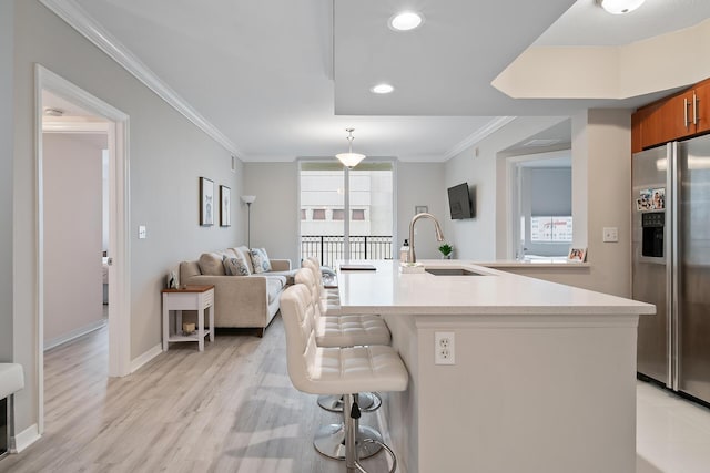 kitchen featuring a center island with sink, stainless steel refrigerator with ice dispenser, sink, a kitchen breakfast bar, and ornamental molding