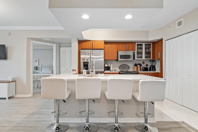 kitchen with a breakfast bar, ornamental molding, stainless steel appliances, and light wood-type flooring