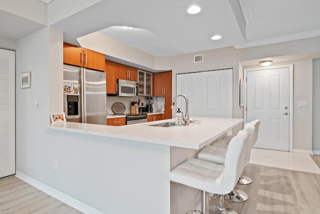 kitchen with appliances with stainless steel finishes, light hardwood / wood-style floors, a kitchen breakfast bar, sink, and kitchen peninsula