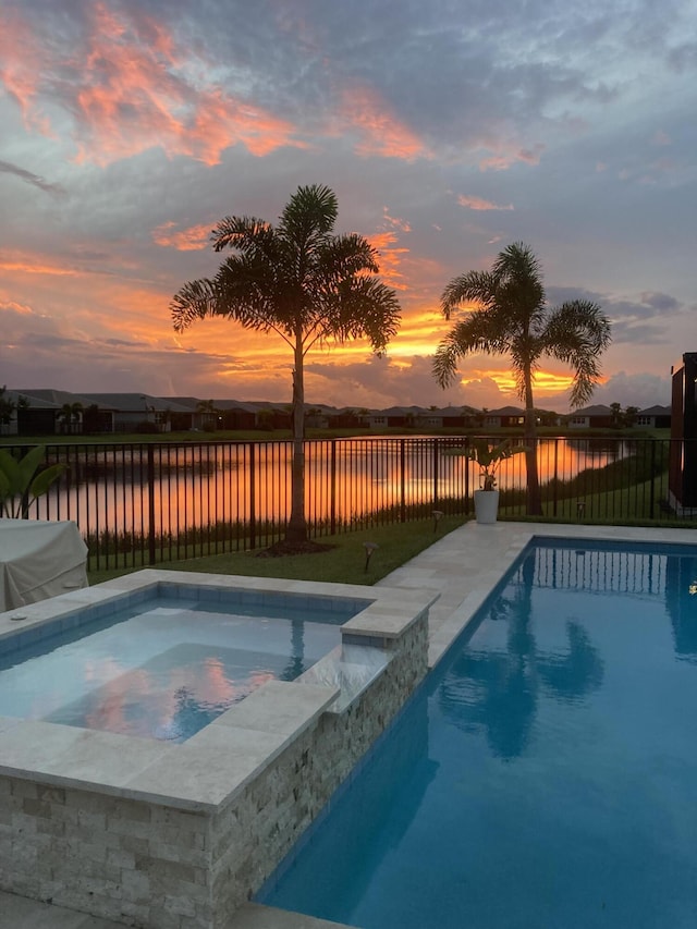 pool at dusk with a water view and an in ground hot tub