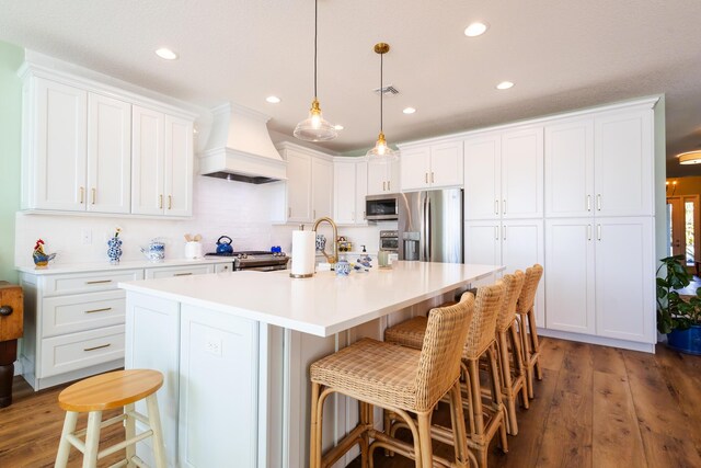 kitchen featuring premium range hood, a kitchen island with sink, appliances with stainless steel finishes, white cabinets, and dark hardwood / wood-style flooring