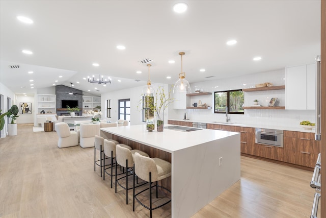 kitchen featuring a spacious island, white cabinets, lofted ceiling, hanging light fixtures, and light hardwood / wood-style flooring