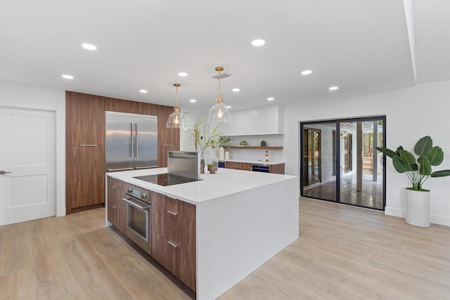 kitchen with decorative light fixtures, stainless steel oven, an island with sink, white cabinets, and black electric cooktop