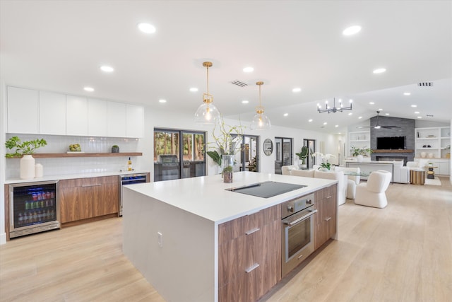 kitchen featuring a center island with sink, wine cooler, oven, vaulted ceiling, and white cabinets