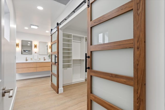 spacious closet with a barn door, sink, and light hardwood / wood-style flooring