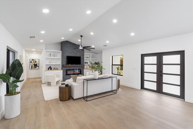 living room with lofted ceiling, built in shelves, light wood-type flooring, and a large fireplace