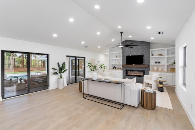 living room featuring built in shelves, light hardwood / wood-style floors, a large fireplace, vaulted ceiling, and ceiling fan