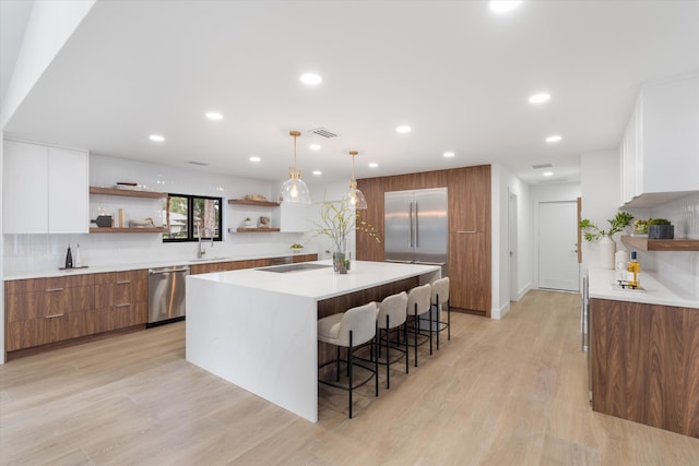 kitchen featuring decorative light fixtures, tasteful backsplash, a kitchen bar, white cabinetry, and appliances with stainless steel finishes