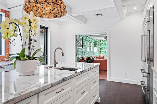 kitchen featuring white cabinetry, sink, light stone countertops, and beamed ceiling