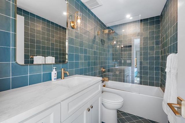 full bathroom with tiled shower / bath, tile walls, vanity, toilet, and tile patterned floors