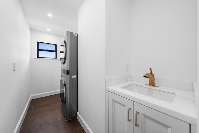 clothes washing area with stacked washing maching and dryer, sink, and dark hardwood / wood-style flooring