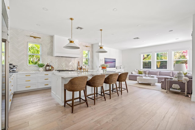 kitchen with a kitchen bar, light stone counters, decorative light fixtures, an island with sink, and white cabinets