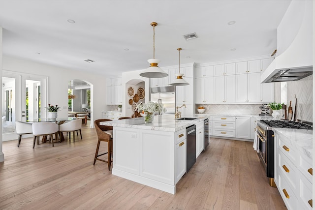 kitchen featuring pendant lighting, premium appliances, extractor fan, an island with sink, and white cabinets