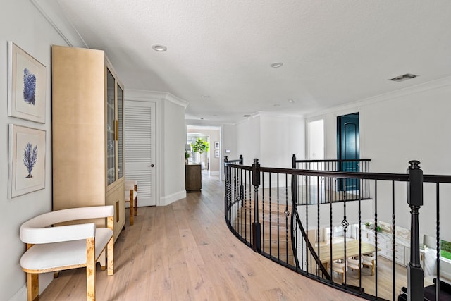 corridor featuring ornamental molding, light hardwood / wood-style floors, and a textured ceiling