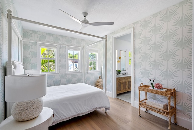 bedroom with ceiling fan, connected bathroom, light hardwood / wood-style flooring, and a textured ceiling