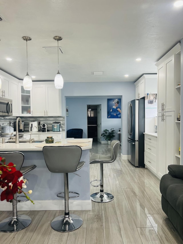 kitchen with stainless steel appliances, backsplash, white cabinets, and decorative light fixtures