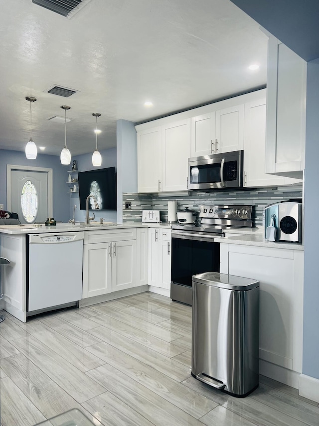 kitchen featuring white cabinets, backsplash, stainless steel appliances, and pendant lighting