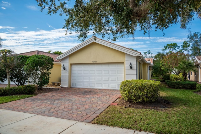 view of front of home with a garage, a tile roof, decorative driveway, stucco siding, and a front lawn