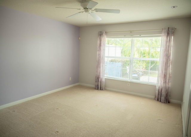 carpeted spare room featuring plenty of natural light, baseboards, and ceiling fan