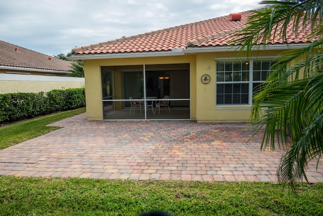 back of house featuring a patio, a tiled roof, a sunroom, and stucco siding