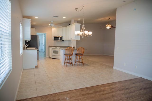 kitchen featuring a breakfast bar area, ceiling fan with notable chandelier, a sink, white cabinetry, and appliances with stainless steel finishes