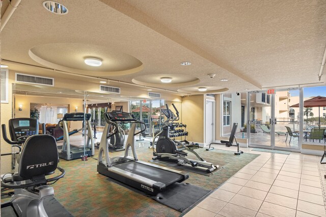 workout area featuring expansive windows, a tray ceiling, tile patterned flooring, and a textured ceiling