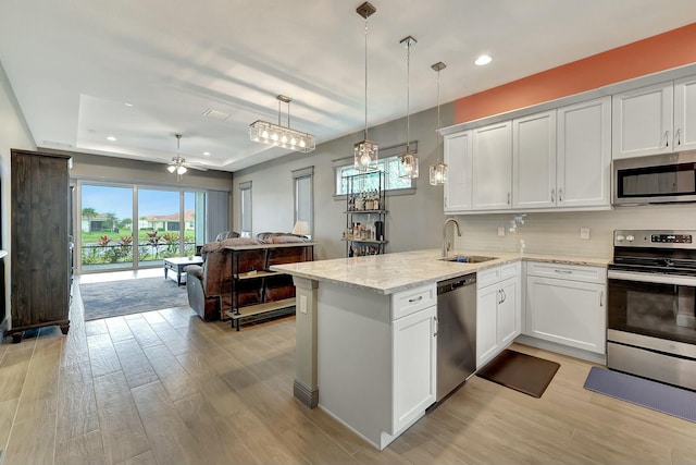 kitchen with appliances with stainless steel finishes, white cabinetry, sink, a raised ceiling, and kitchen peninsula