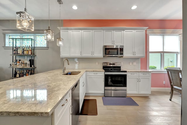 kitchen featuring stainless steel appliances, light stone countertops, pendant lighting, white cabinets, and sink