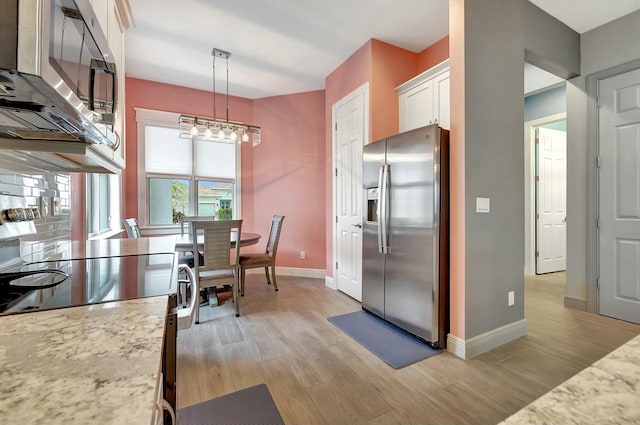 kitchen featuring decorative light fixtures, white cabinetry, light hardwood / wood-style flooring, light stone countertops, and appliances with stainless steel finishes