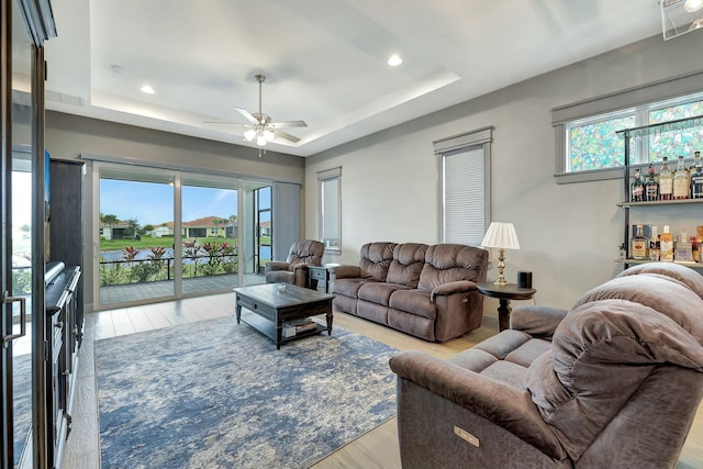 living room with light wood-type flooring, ceiling fan, plenty of natural light, and a raised ceiling