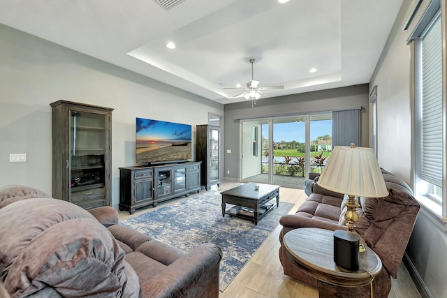 living room featuring ceiling fan, a raised ceiling, and light wood-type flooring