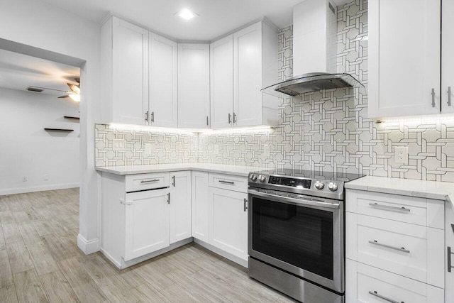 kitchen with light hardwood / wood-style floors, decorative backsplash, stainless steel electric range, wall chimney exhaust hood, and white cabinets