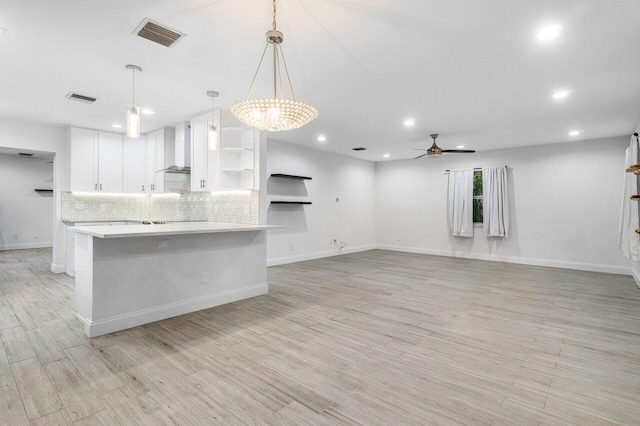 kitchen with decorative backsplash, hanging light fixtures, white cabinets, wall chimney exhaust hood, and ceiling fan with notable chandelier