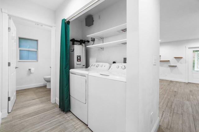 laundry room featuring water heater, light hardwood / wood-style floors, and washer and clothes dryer