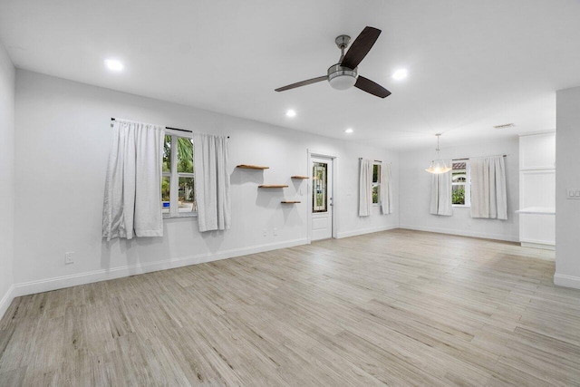 unfurnished living room featuring ceiling fan with notable chandelier and light hardwood / wood-style floors