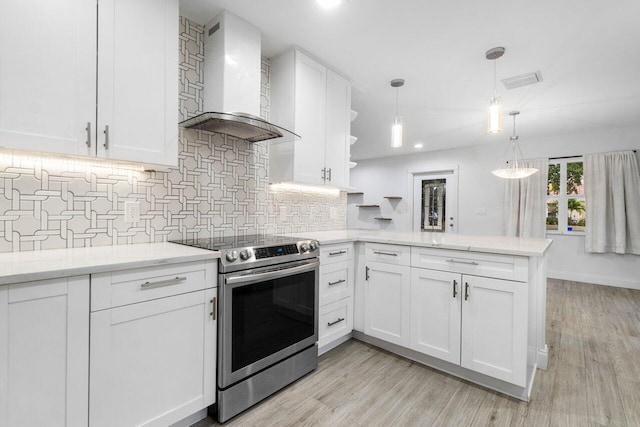 kitchen with stainless steel electric stove, wall chimney range hood, white cabinetry, hanging light fixtures, and kitchen peninsula