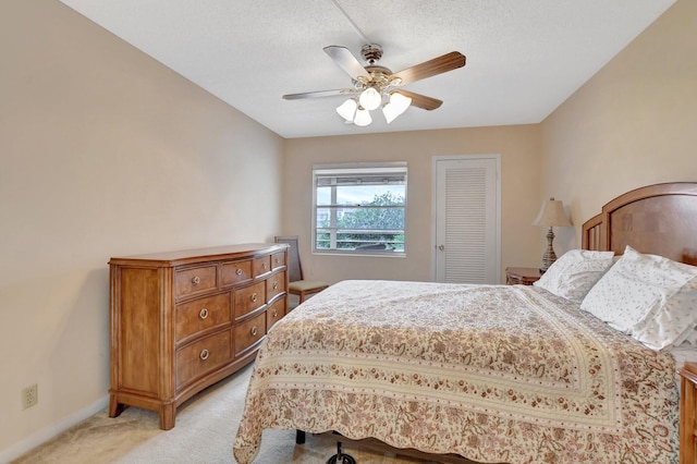 bedroom featuring a textured ceiling, ceiling fan, a closet, and light colored carpet