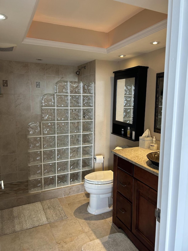 bathroom with toilet, vanity, a tray ceiling, and a tile shower