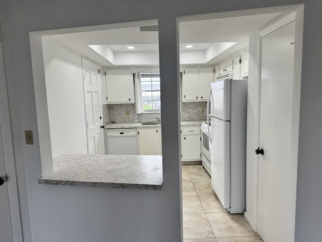 kitchen featuring backsplash, white appliances, white cabinets, and a raised ceiling