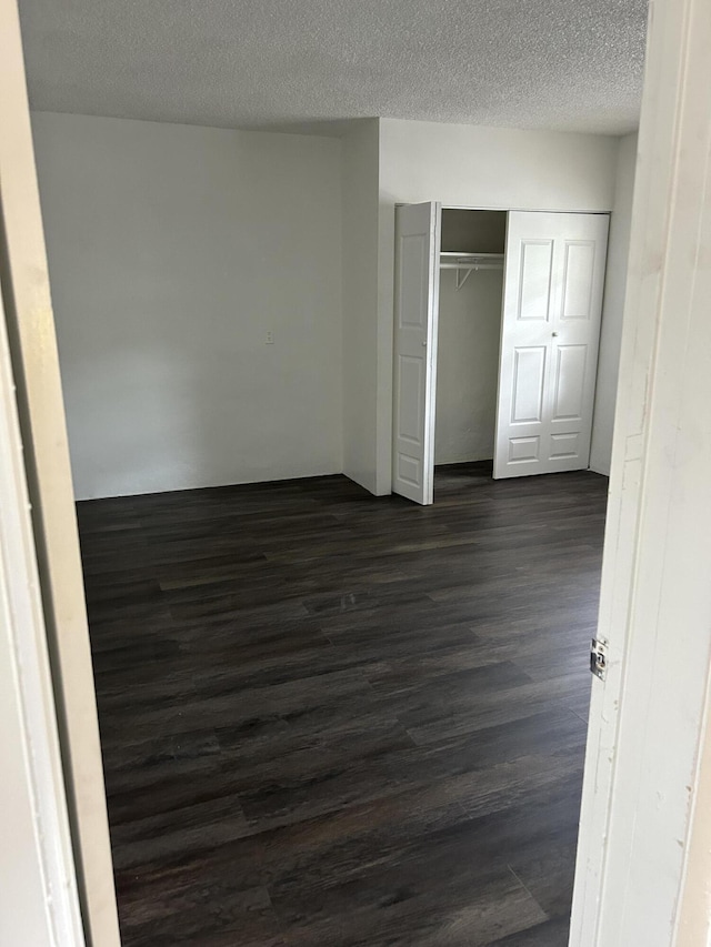 unfurnished bedroom with a textured ceiling, a closet, and dark hardwood / wood-style floors