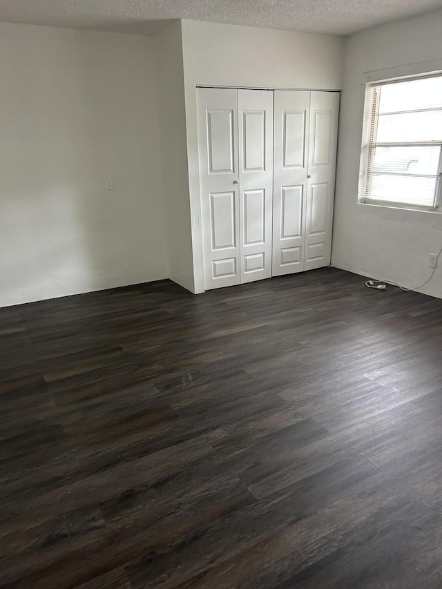 unfurnished bedroom featuring dark wood-type flooring, a textured ceiling, and a closet