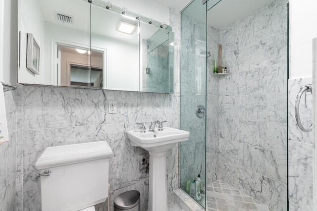 bathroom featuring toilet, tile walls, a shower with shower door, and sink