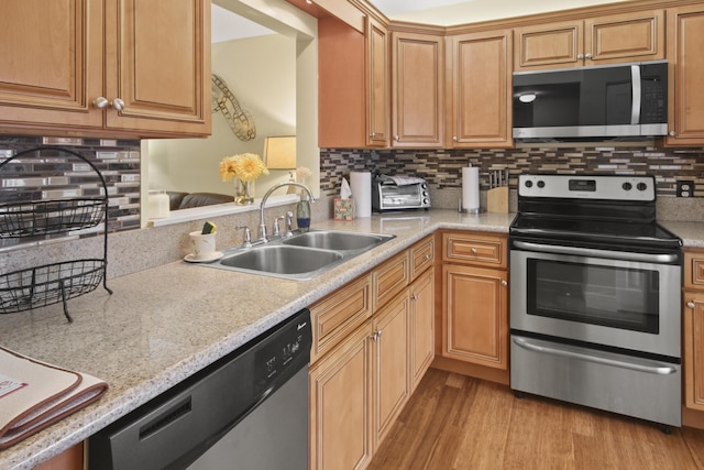 kitchen featuring appliances with stainless steel finishes, backsplash, light stone countertops, light hardwood / wood-style flooring, and sink