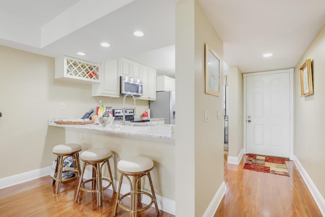 kitchen featuring white cabinetry, stainless steel appliances, light hardwood / wood-style floors, light stone counters, and a breakfast bar