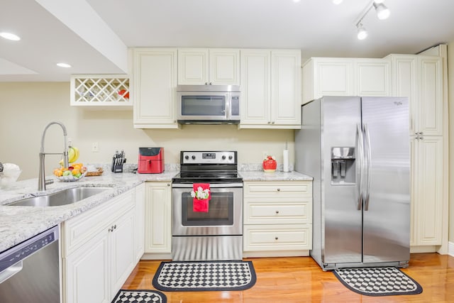 kitchen featuring sink, light wood-type flooring, light stone countertops, stainless steel appliances, and white cabinets