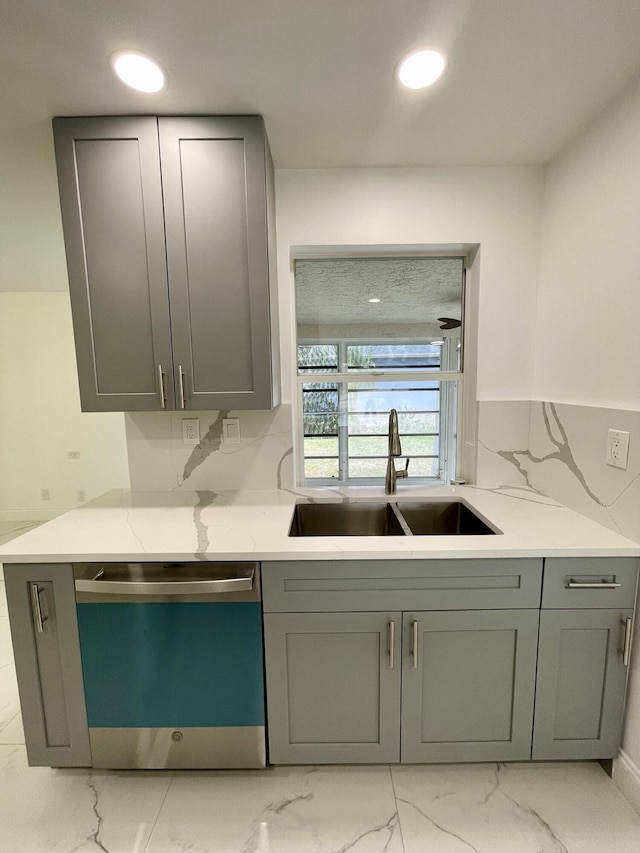 kitchen featuring stainless steel dishwasher, sink, light stone counters, and gray cabinets