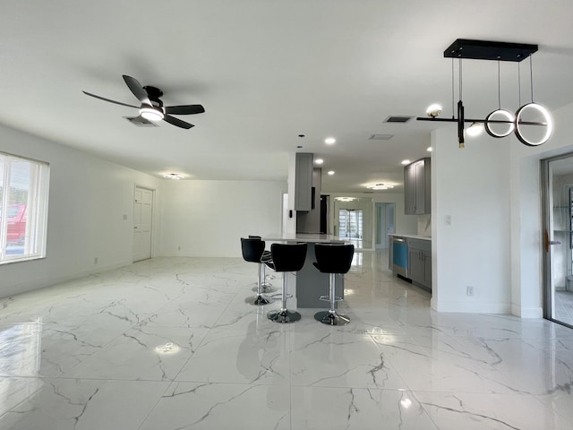 kitchen with decorative light fixtures, ceiling fan, dishwasher, gray cabinetry, and a breakfast bar area