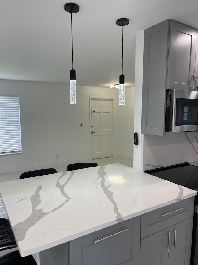 kitchen featuring light stone countertops, pendant lighting, and gray cabinets