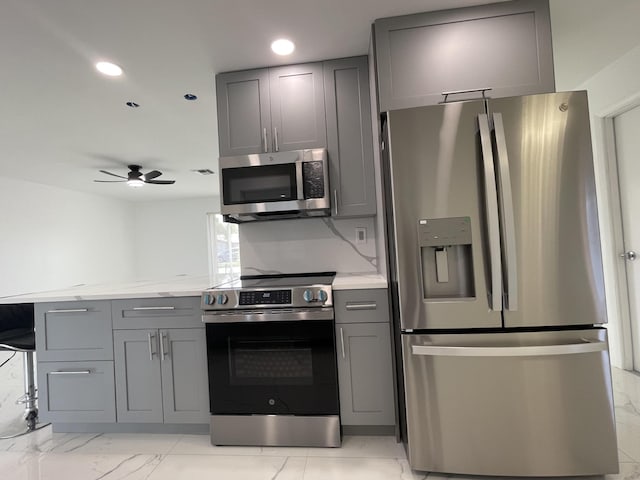 kitchen featuring ceiling fan, appliances with stainless steel finishes, gray cabinetry, and decorative backsplash