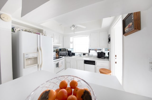 kitchen featuring ceiling fan, sink, a tray ceiling, white appliances, and white cabinetry